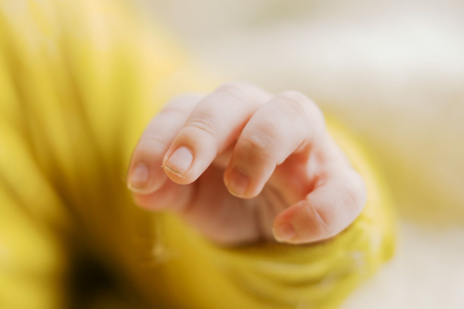 Close-up of a newborn baby's tiny hand with delicate fingers, wearing a yellow outfit.