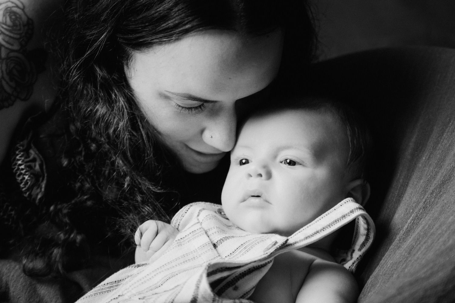 Black and white photo of a mother tenderly gazing at her newborn baby wrapped in a striped onesie.