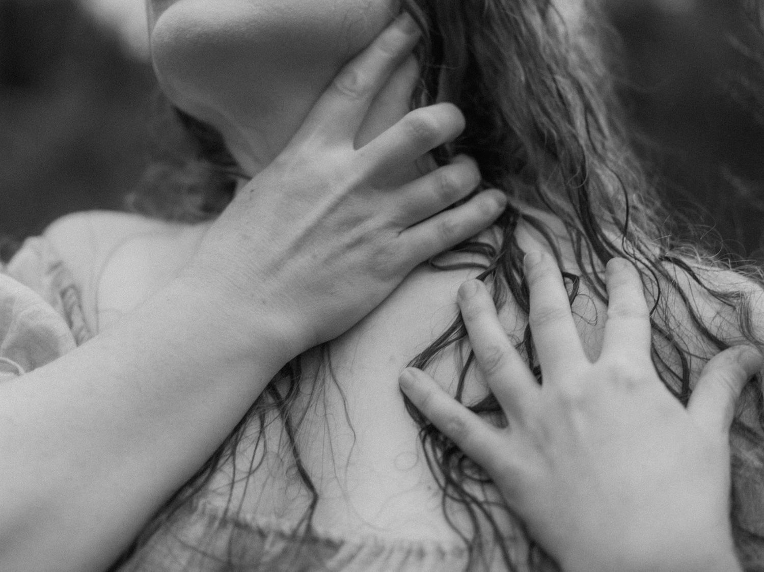 Black and white photo of hands gently resting on a young woman's chest and neck, artistic portrait photography.
