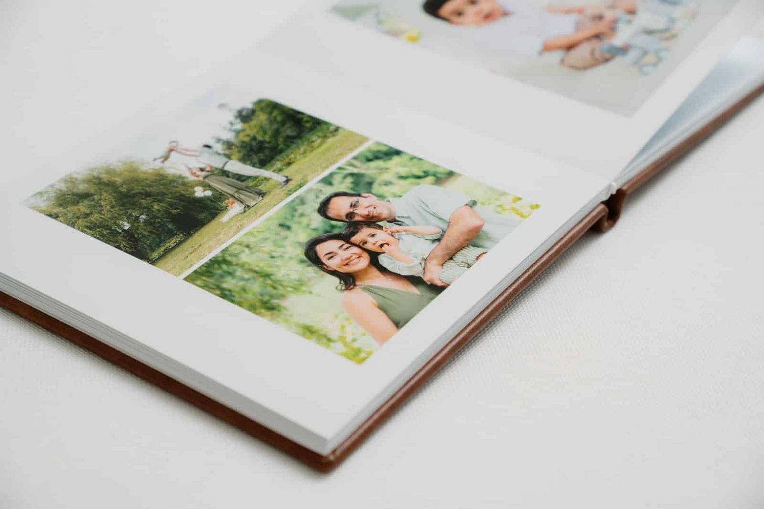 Open photo album displaying family portrait photos on white pages, showcasing outdoor memories in a hardcover book.