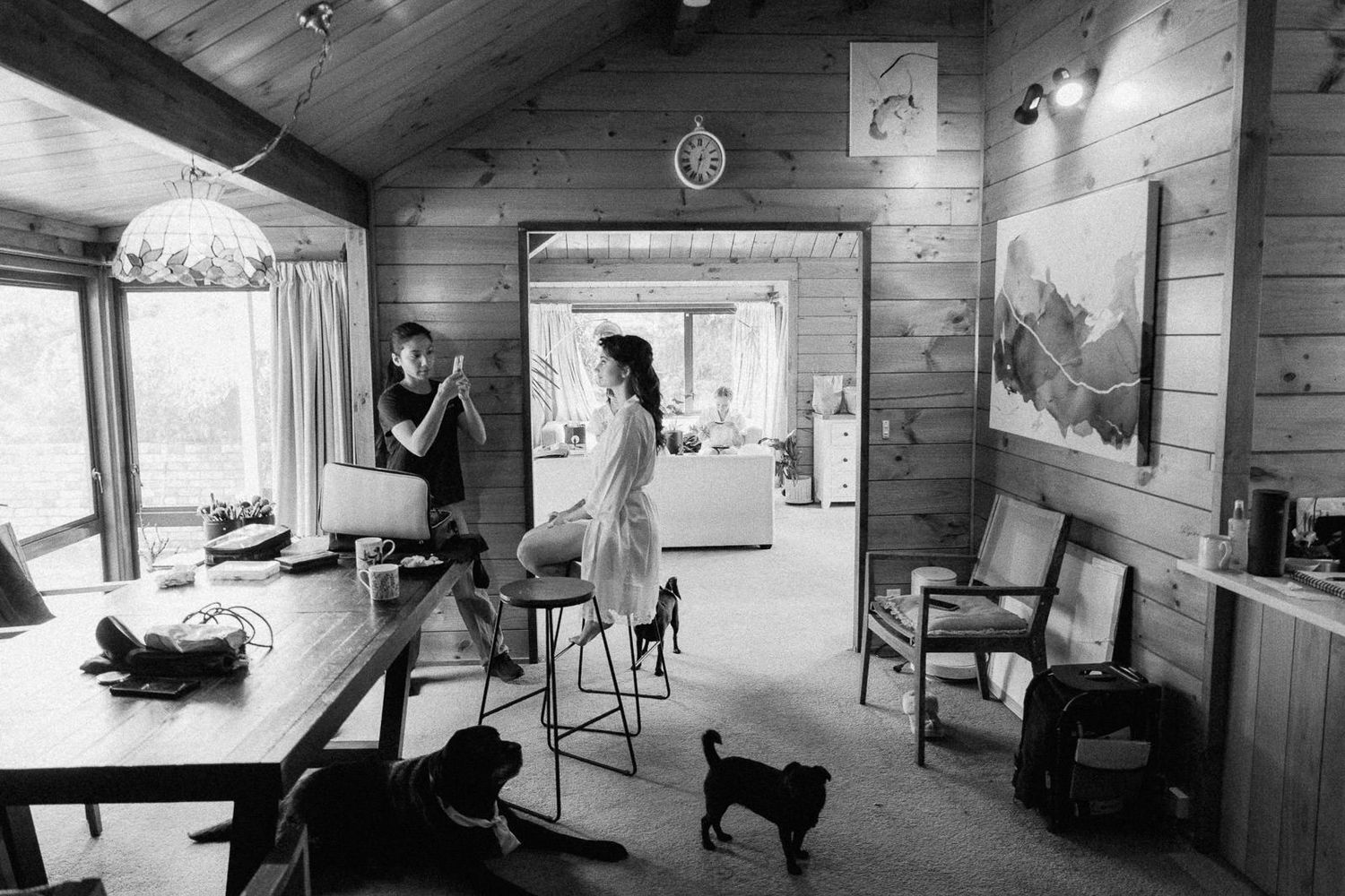 Black and white photo of two women in a rustic wood-paneled cabin with two dogs resting on the floor.