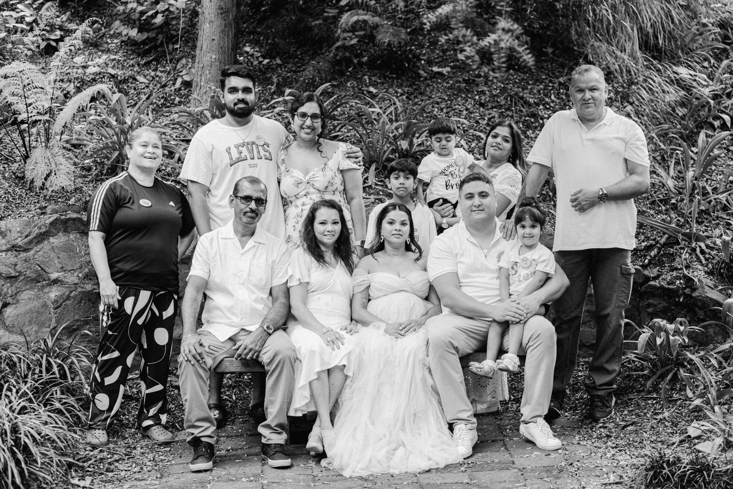 Black and white family portrait outdoors with adults and children posing together, one woman in a white dress appears pregnant.