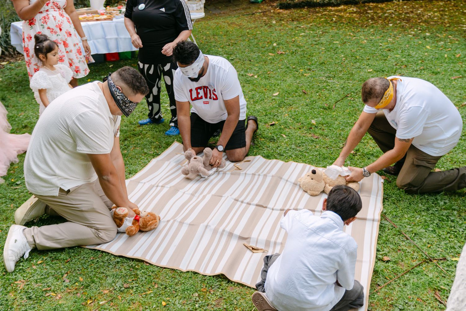 Group of people wearing masks practicing CPR on mannequins during an outdoor first aid training session on a blanket.