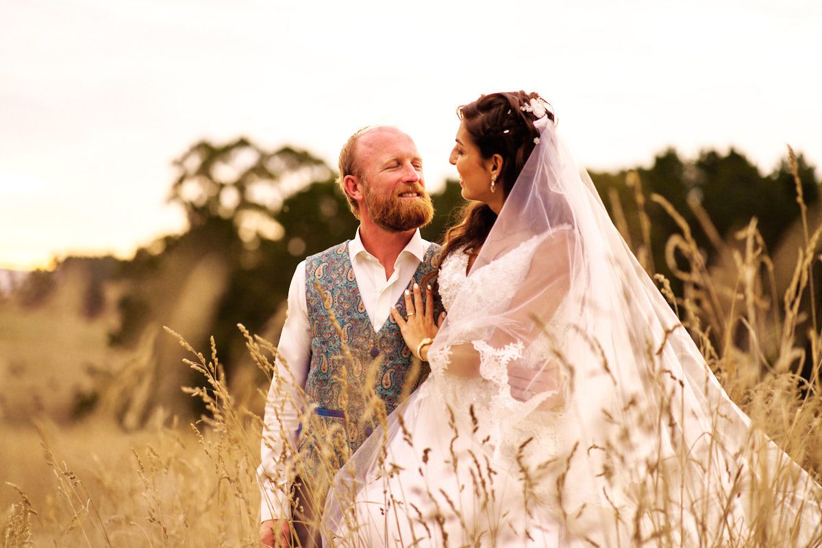 A bride and groom share a romantic moment in a golden field at sunset, with the bride wearing a flowing veil.