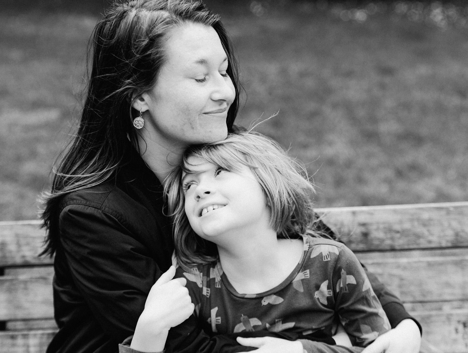 Black and white photo of a mother and child sharing a tender moment on a bench outdoors.
