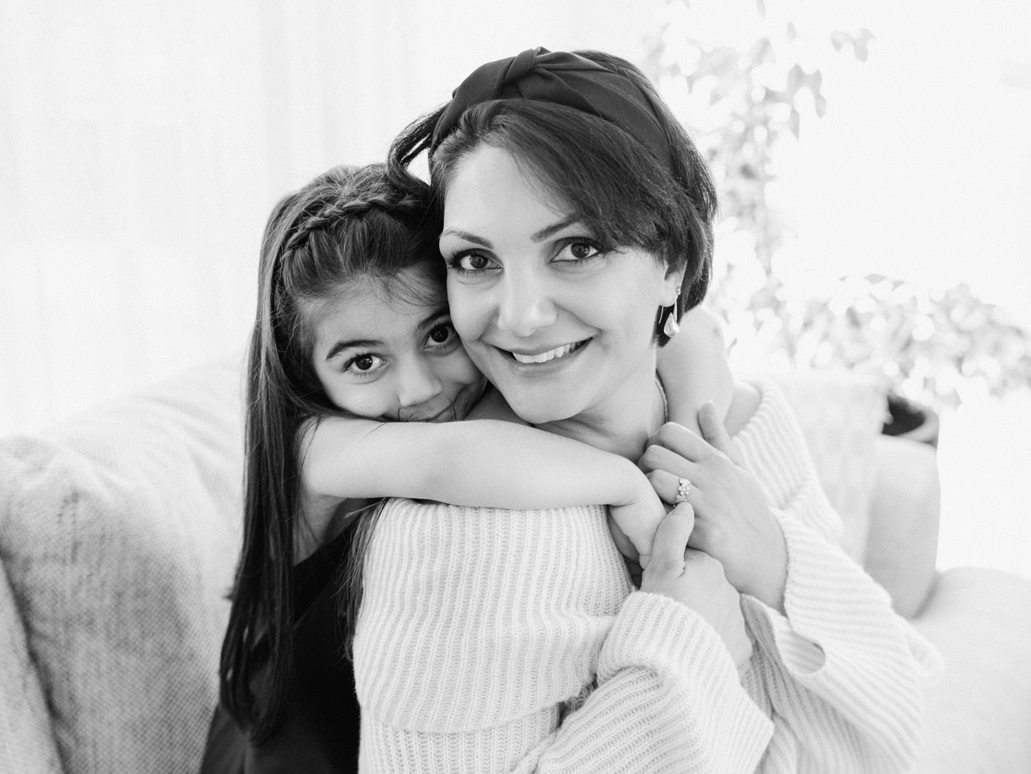 Black and white photo of a smiling woman and young girl hugging warmly on a couch.