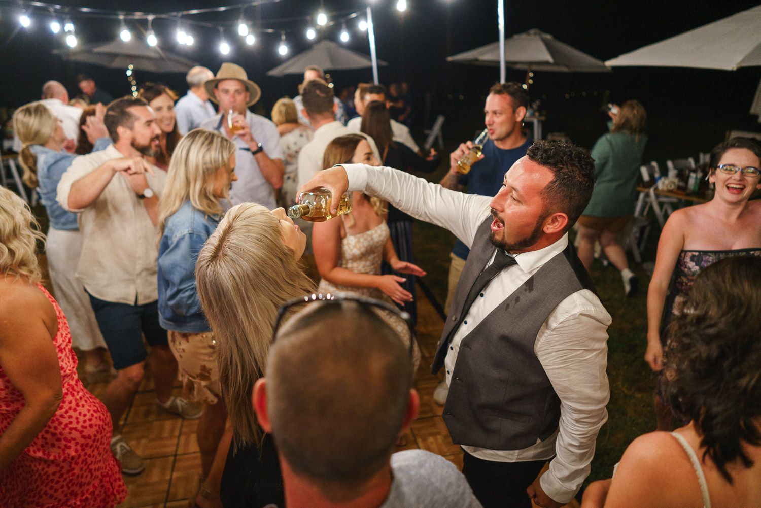 Guests dancing and celebrating at an outdoor wedding reception under string lights at night.