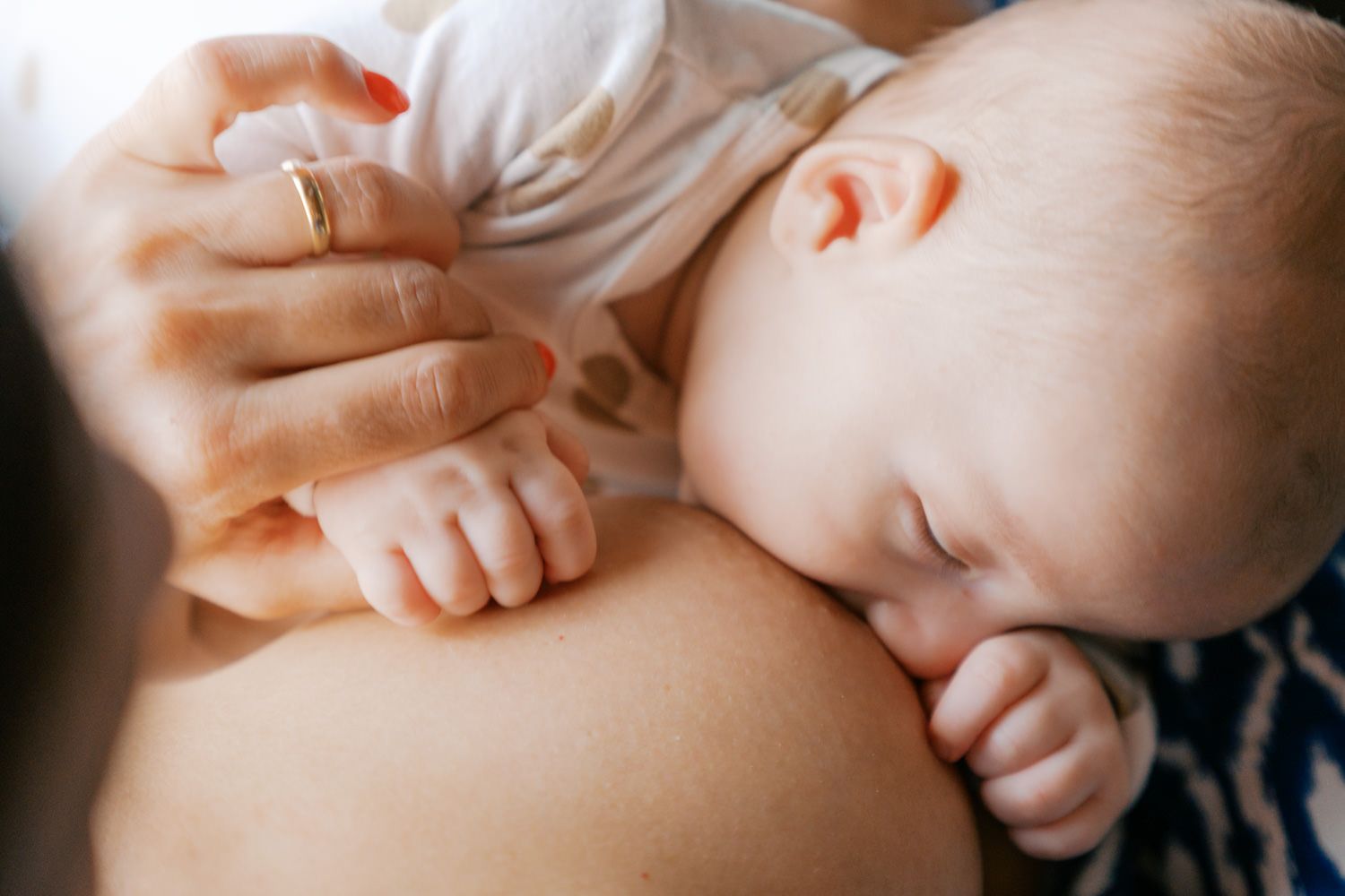 Close-up of a sleeping newborn baby breastfeeding, with mother's hand gently supporting the infant.