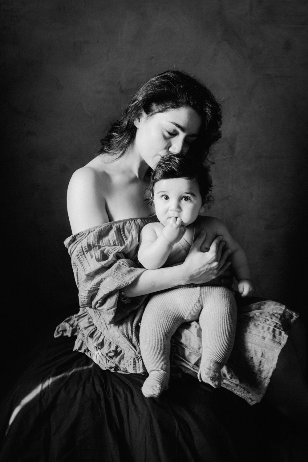 Black and white portrait of a mother tenderly holding her baby, studio photography.
