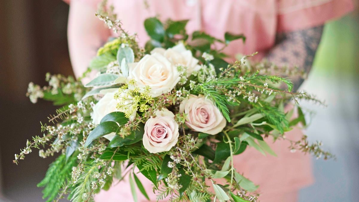 Elegant bridal bouquet featuring soft pink and white roses with lush greenery held by a bridesmaid.
