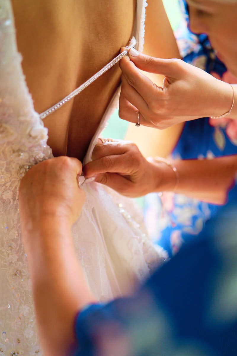 Bridesmaids helping bride lace up the back of her white wedding dress before the ceremony.
