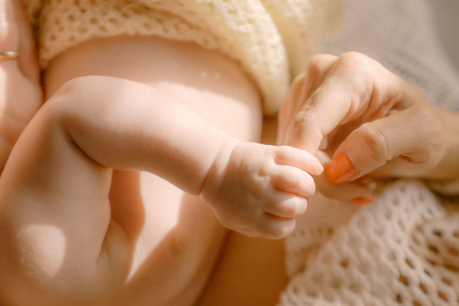 Close-up of a newborn baby's tiny hand gently held by a mother with orange painted nails.