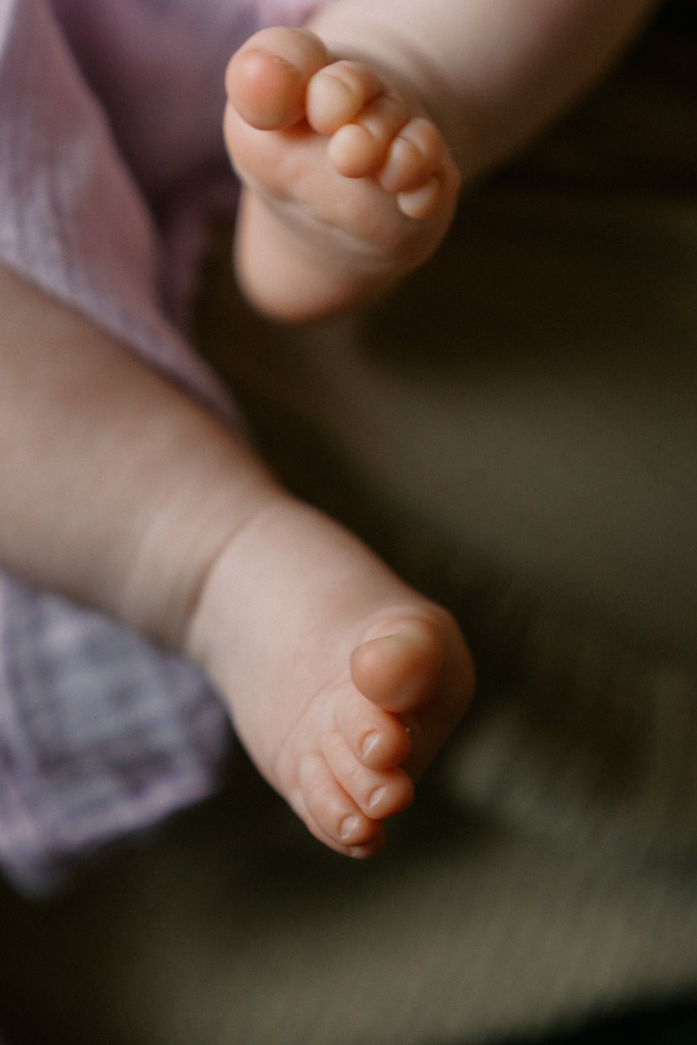 Close-up of tiny newborn baby feet resting on a dark green surface, with a soft purple blanket in the background.