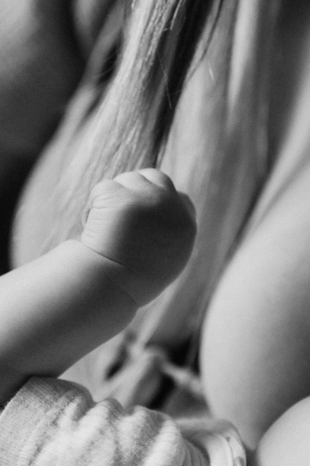 Black and white close-up of a newborn baby's tiny fist clenched near a mother's chest.