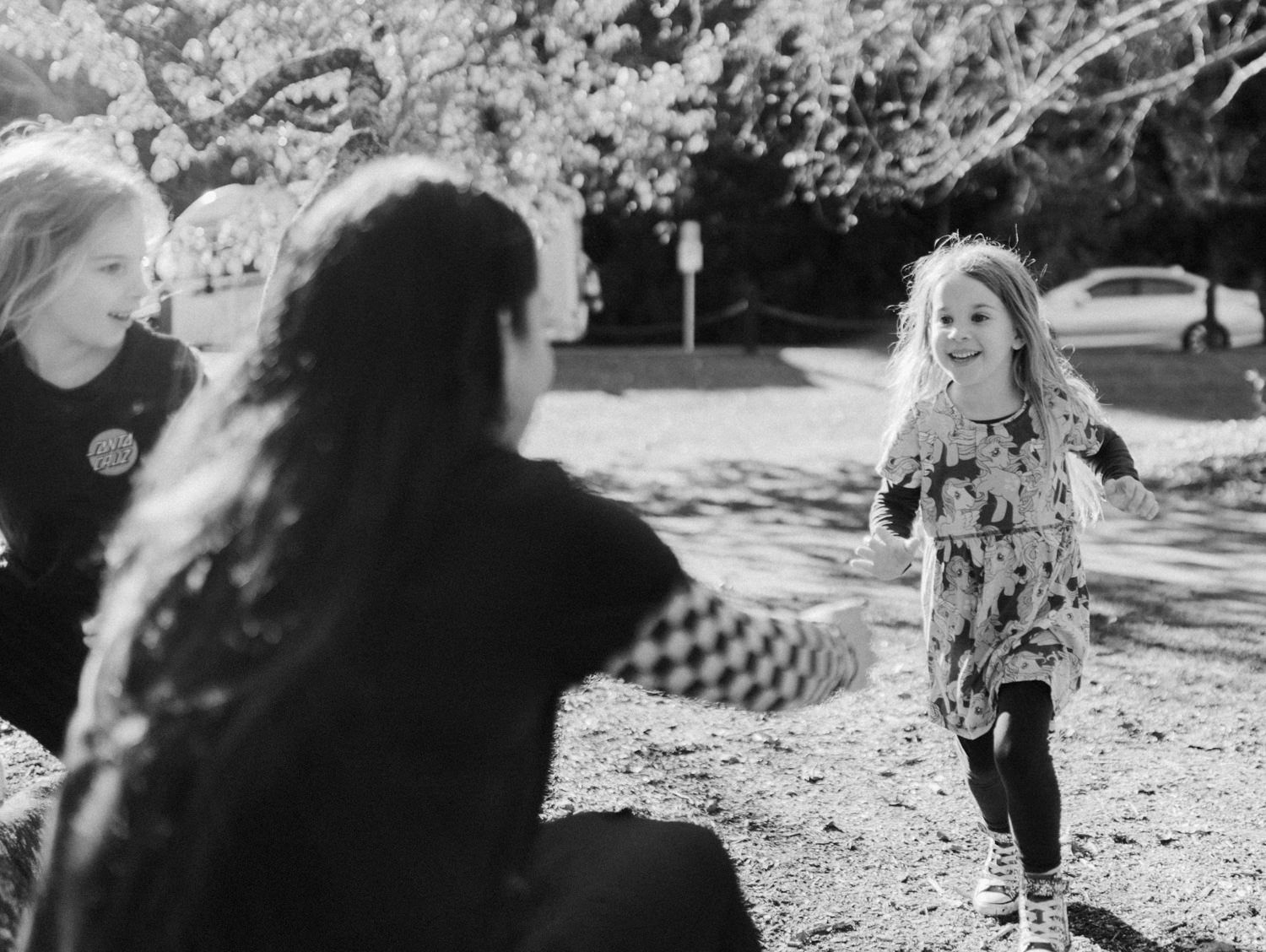 Black and white photo of two adults watching a young girl smile and pose in a park.