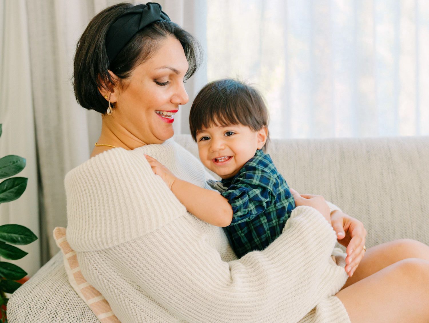 Mother in cream sweater lovingly holding her smiling baby boy.