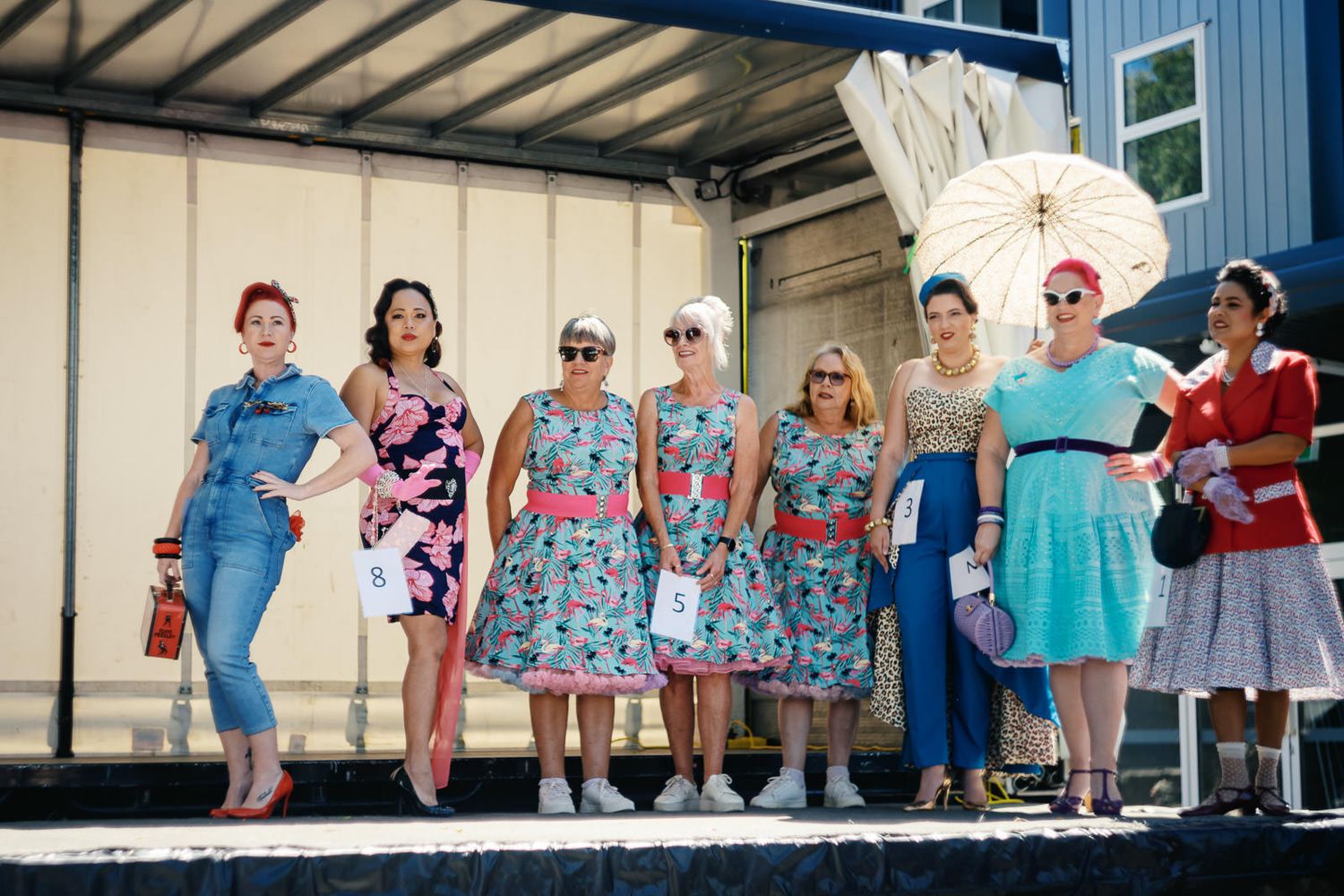 Group of women in vintage 1950s-style dresses posing together outdoors at a retro fashion event.