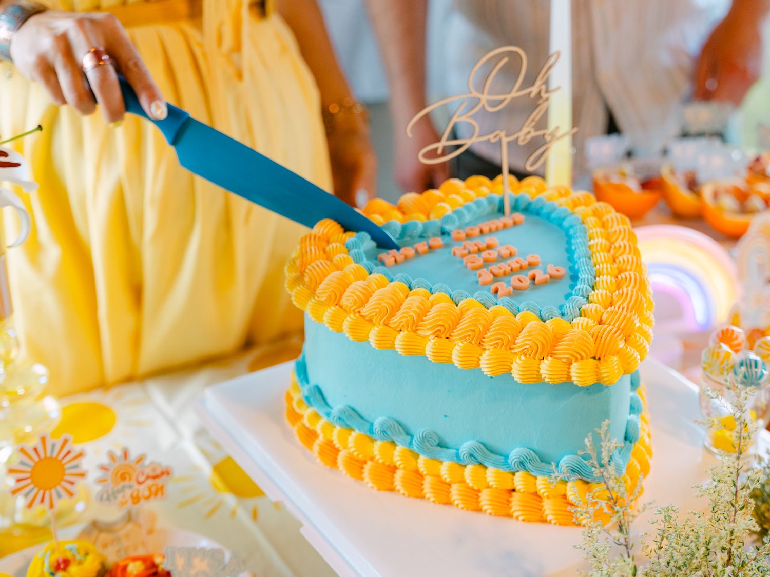A heart-shaped blue and yellow birthday cake being cut with a blue knife at a festive celebration.