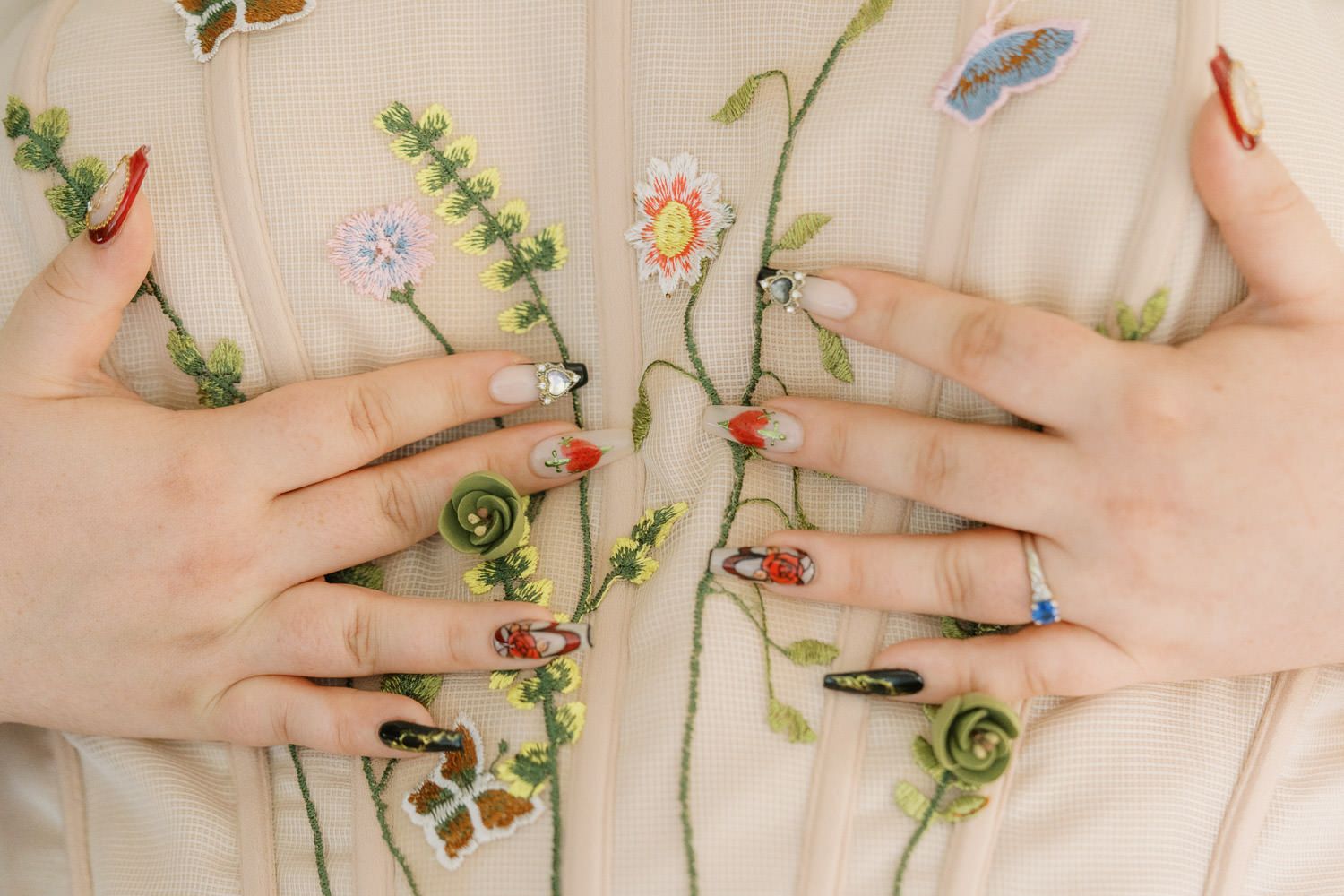 Close-up of hands with floral nail art resting on a white embroidered floral jacket with colorful botanical designs.