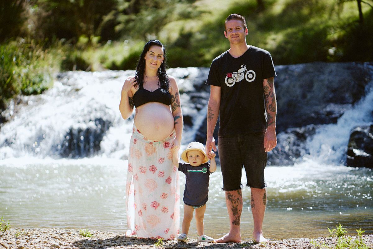 Pregnant woman with family beside waterfall, maternity photo session outdoors.
