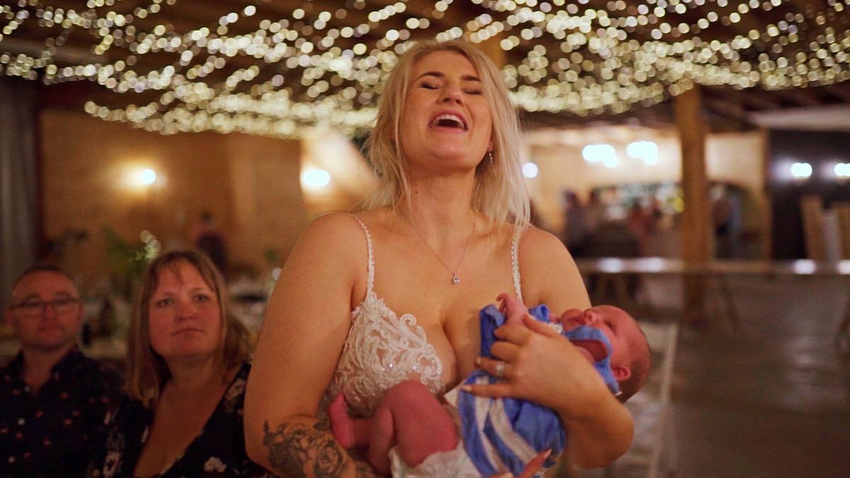 A laughing blonde woman holds a newborn baby at a warmly lit celebration event with fairy lights.