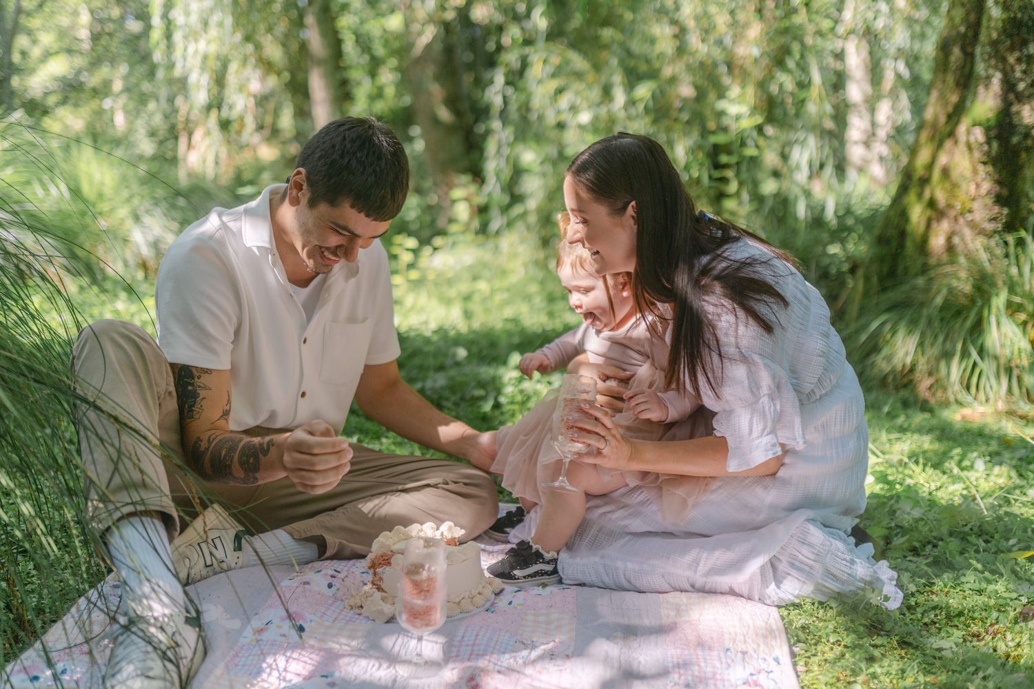 A young family enjoys a peaceful outdoor picnic on a blanket in a lush green forest setting.