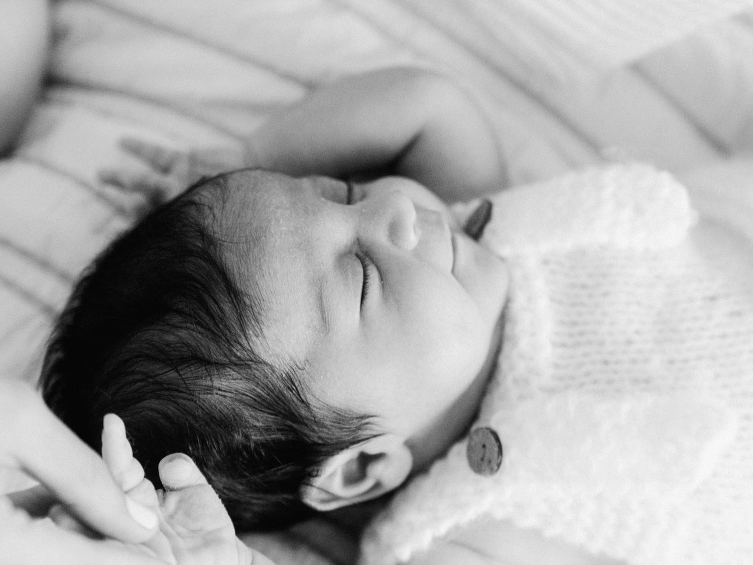 Black and white portrait of sleeping newborn baby in knit outfit with wooden button detail.