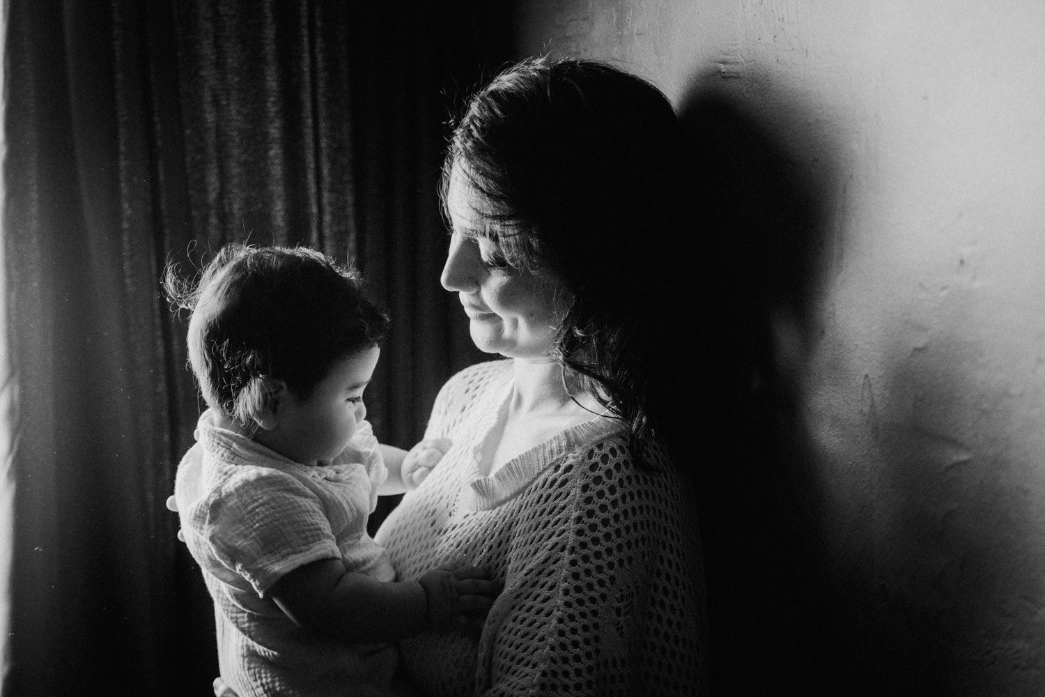 Black and white photo of a mother tenderly holding her baby near a window, radiating love and warmth.