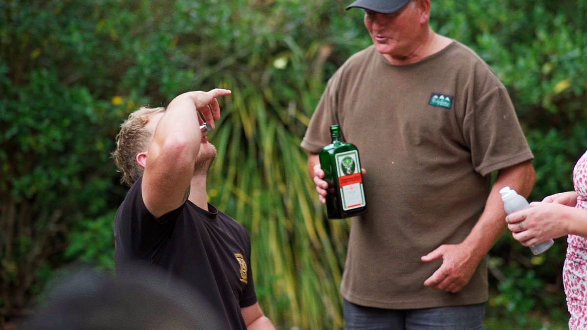 Two men outdoors sharing Jagermeister liquor bottles among green foliage background.