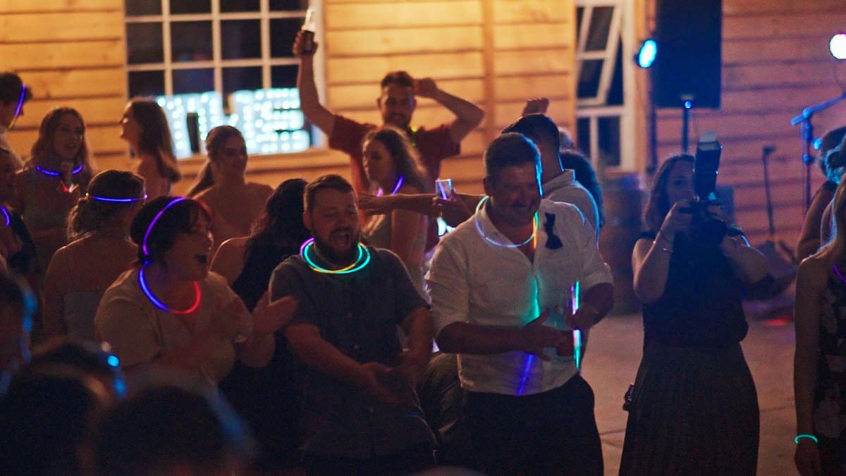 People dancing at an outdoor night party wearing glowing LED necklaces and headbands.