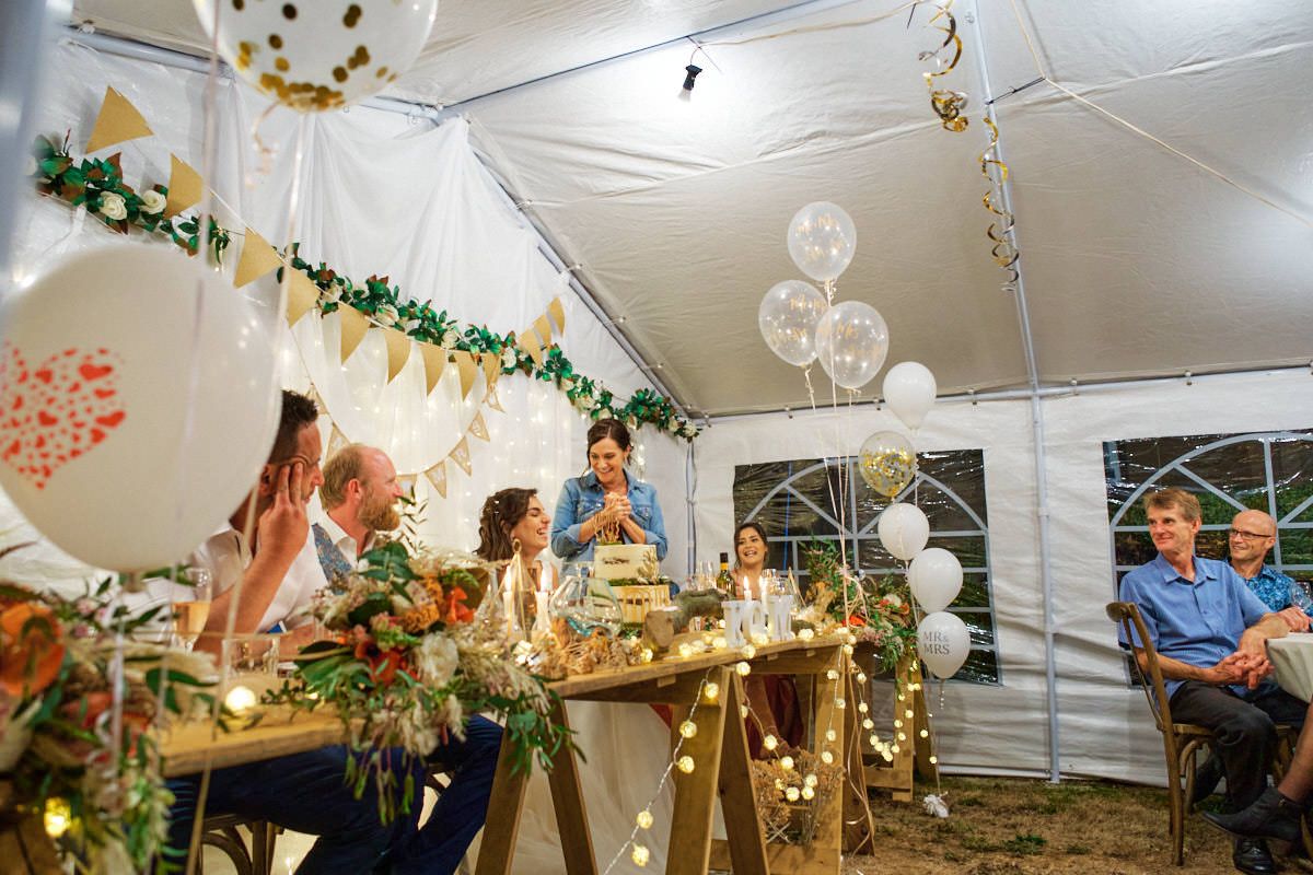 Family celebrating birthday under decorated tent with balloons, fairy lights, and greenery garlands at night.