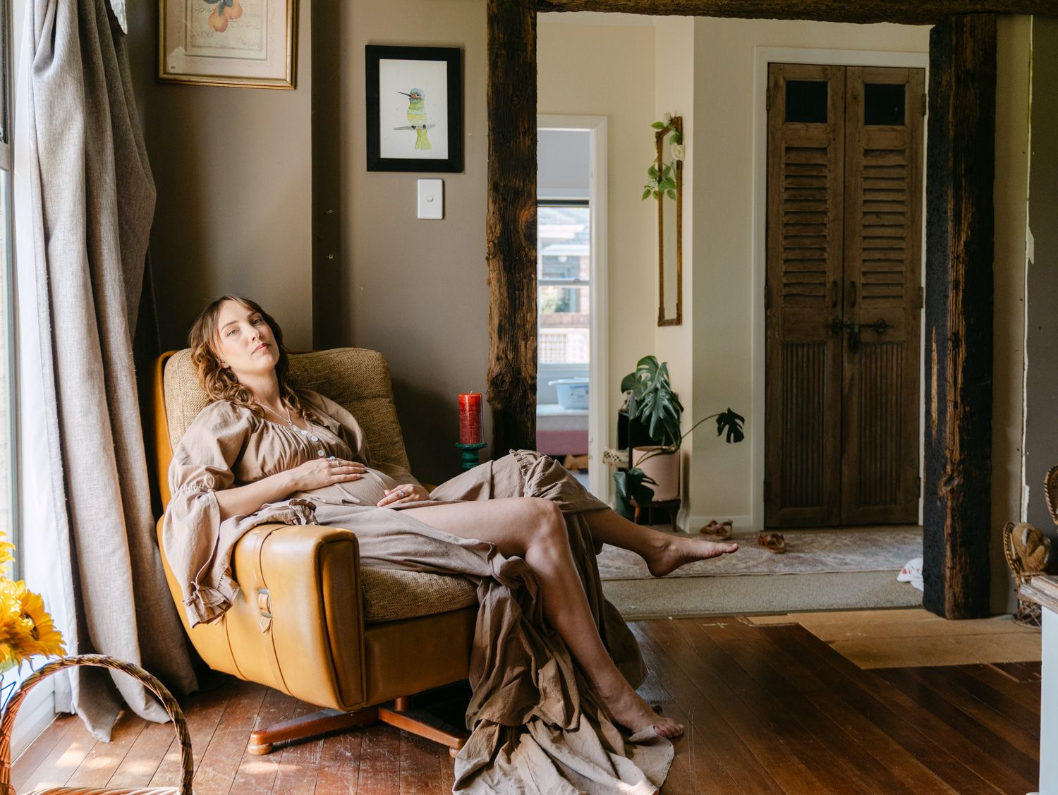 A woman relaxes in a vintage yellow armchair draped with a linen blanket in a cozy, rustic living room.
