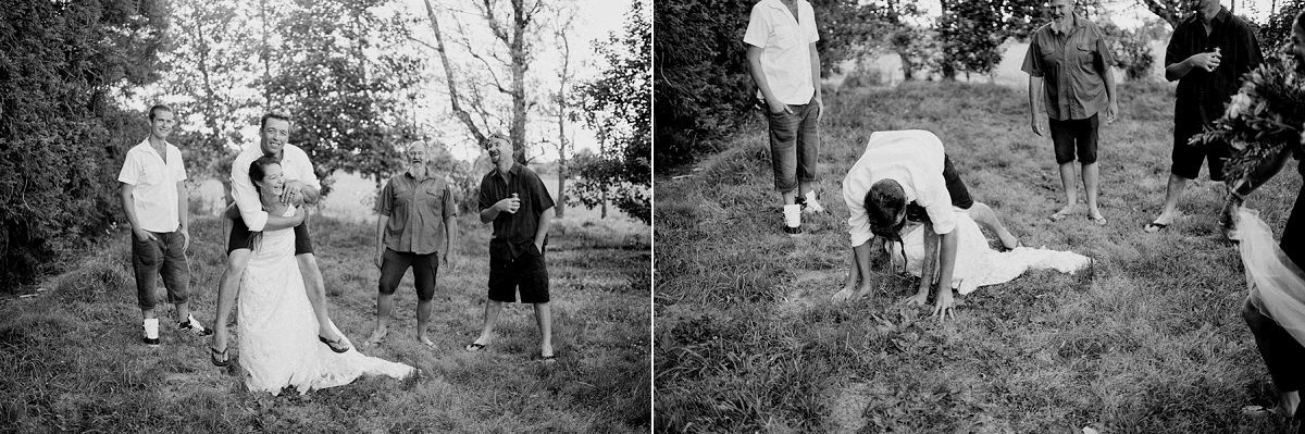 Black and white wedding photo of bride and groom with guests on a grassy hill, capturing candid outdoor celebration moments.