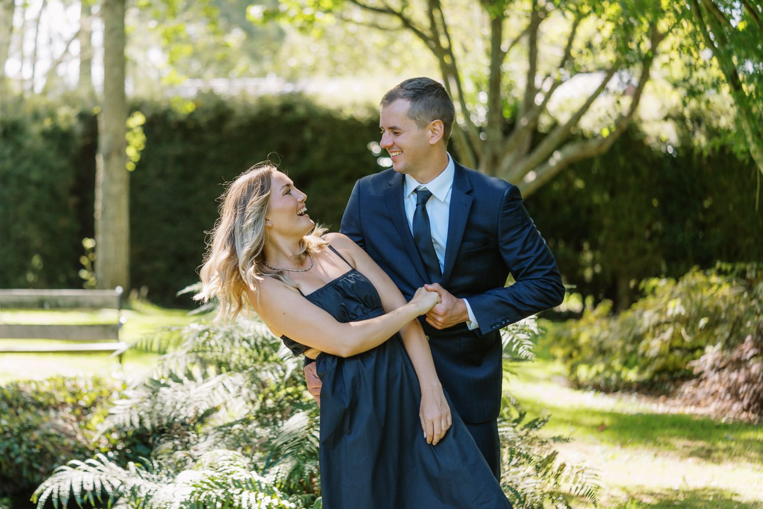 Couple in matching navy outfits dancing and smiling at each other in a lush green garden setting.