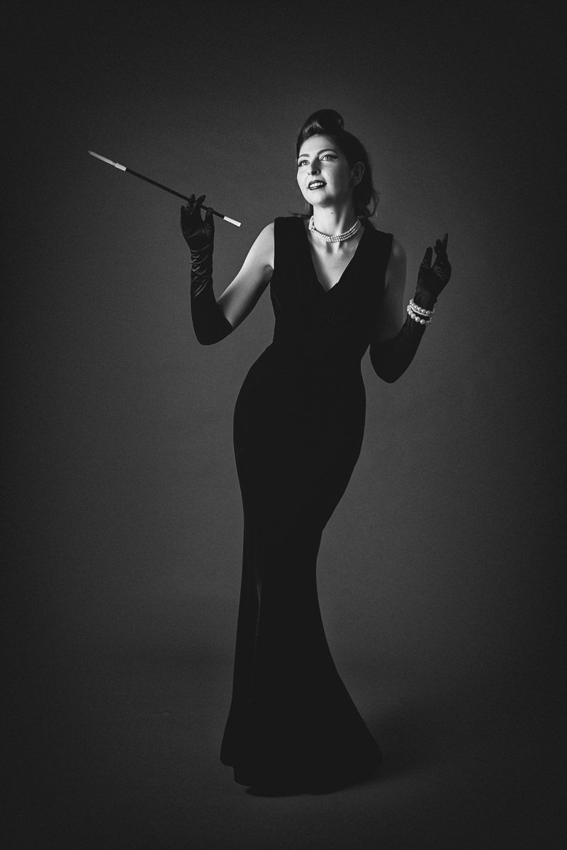Elegant woman in black gown holding cigarette holder, black and white vintage glamour portrait.