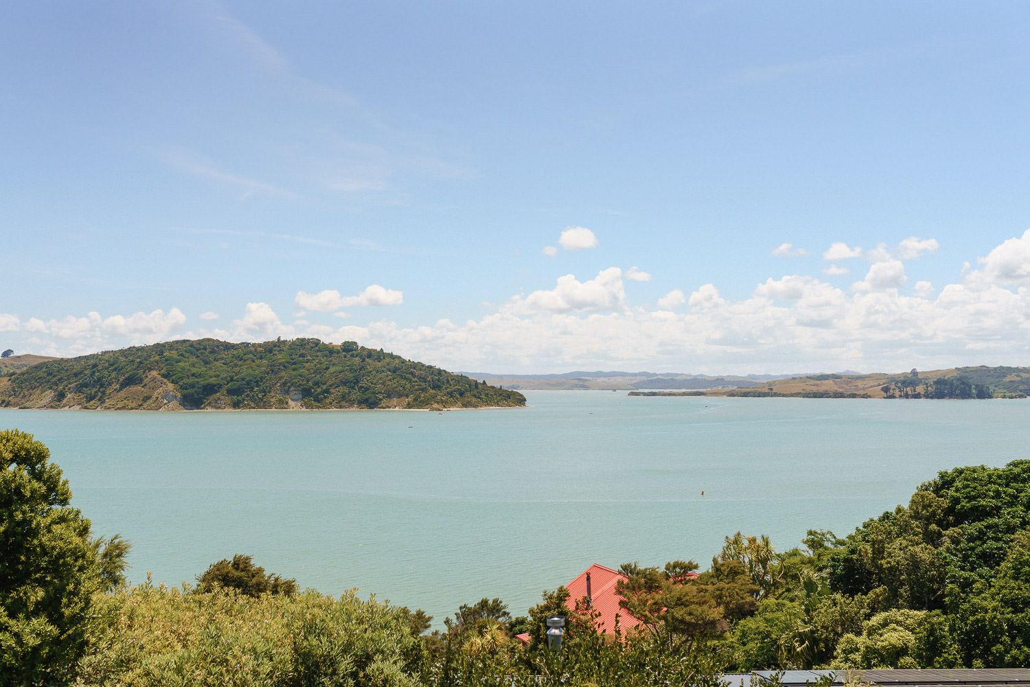 Panoramic view of turquoise harbor waters surrounded by lush green hills under a blue sky with scattered clouds.