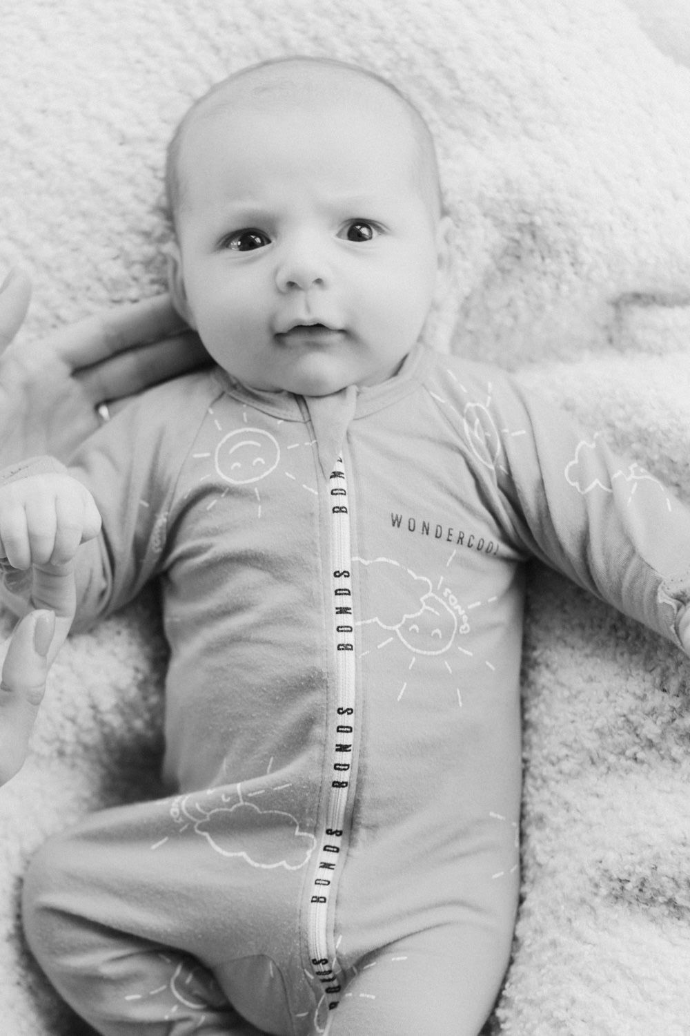 Black and white photo of a newborn baby wearing a Bonds Wondercrew zip romper, lying on a soft white blanket.