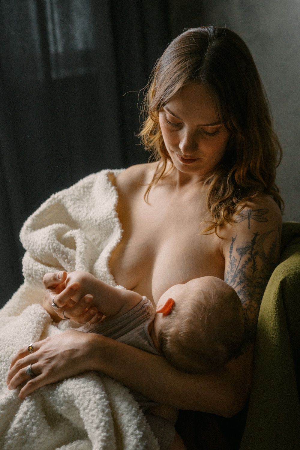 A mother tenderly breastfeeding her newborn baby while wrapped in a soft white blanket, seated in a cozy chair.