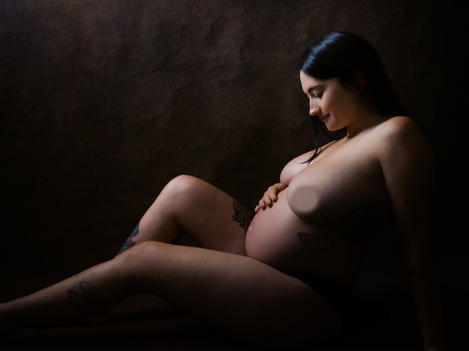 Artistic maternity portrait of a pregnant woman in a dark studio setting, showcasing the beauty of pregnancy.