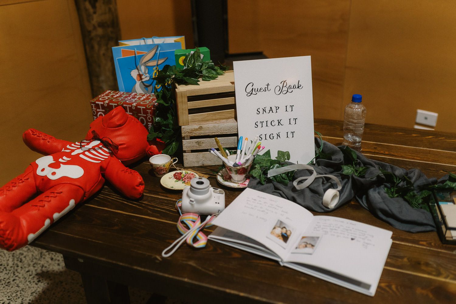 Wedding guest book display table with sign reading Snap It Stick It Sign It, surrounded by decorative items and greenery.