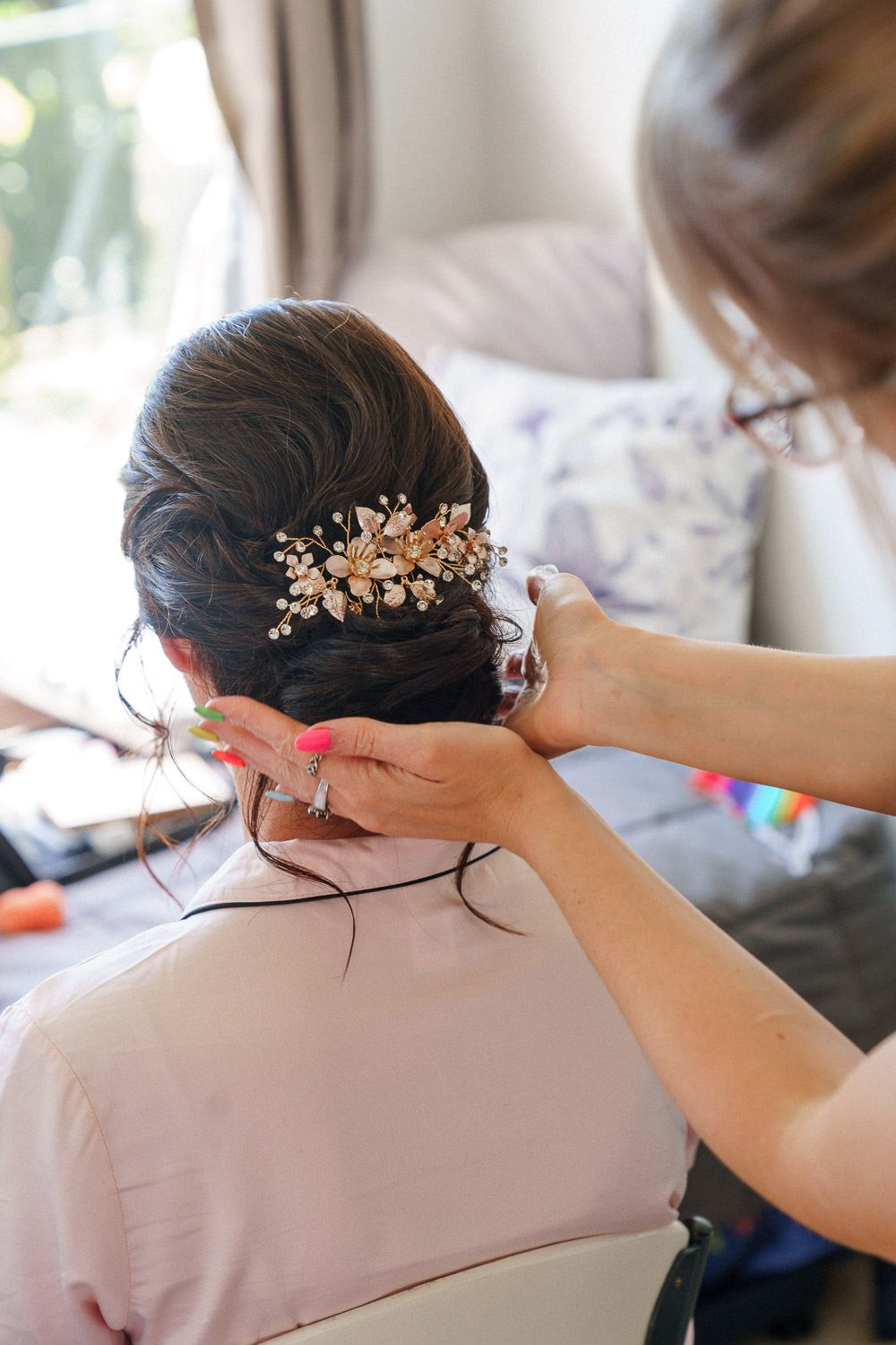 Hairstylist placing a gold floral hair comb into a bride's elegant dark updo hairstyle.