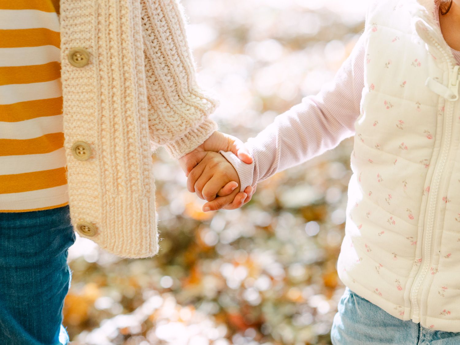 Two people holding hands outdoors, wearing cozy knit sweaters in autumn, with a blurred bokeh background.
