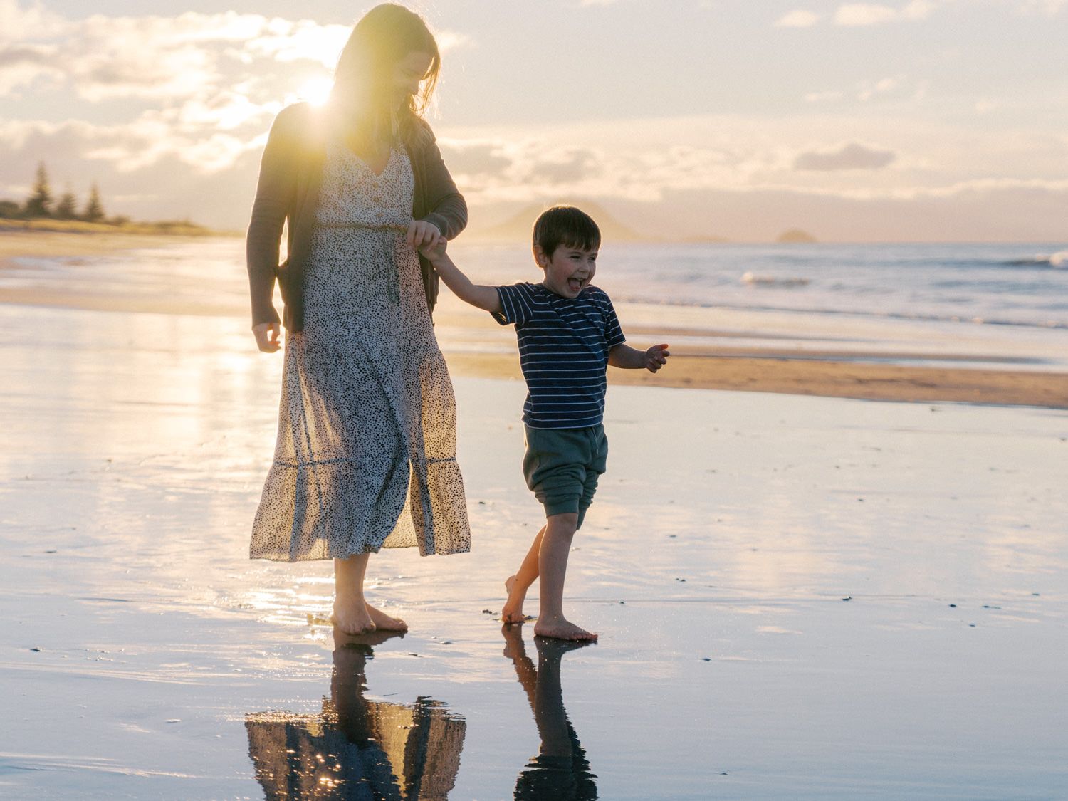 boy holding mums hand and walkingo on wet sand at sunset