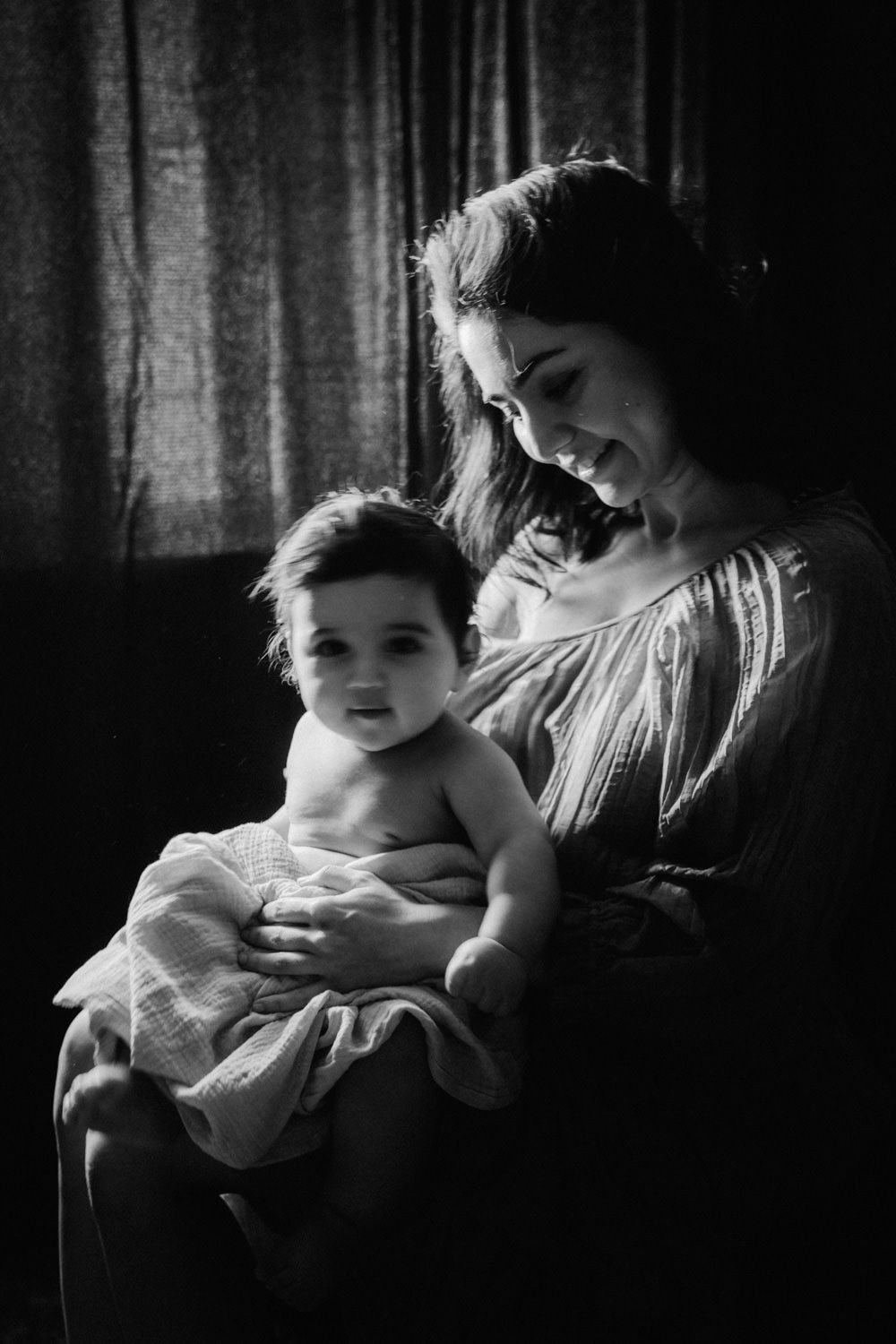 Black and white portrait of a smiling mother lovingly holding her baby wrapped in a soft blanket.