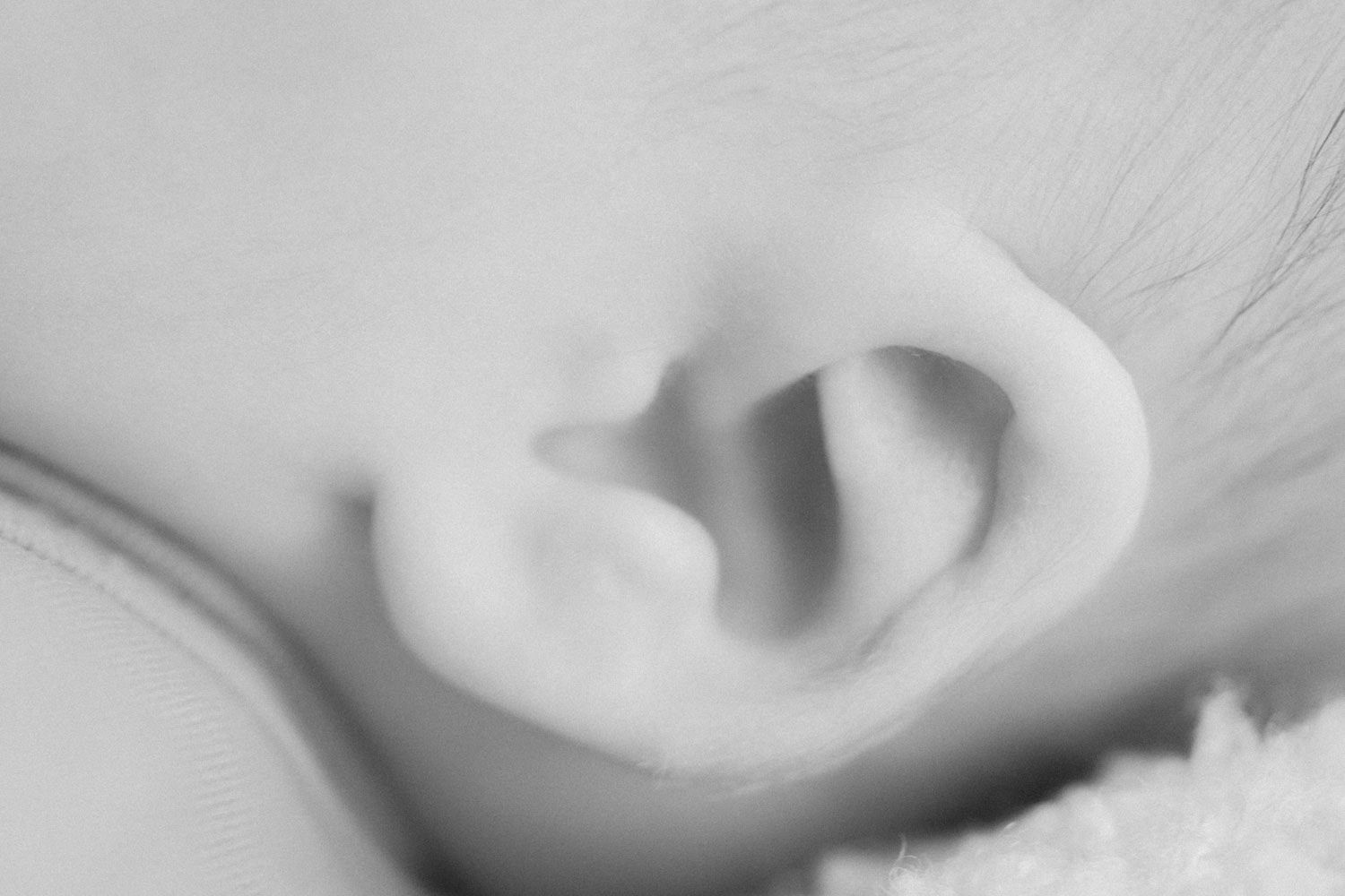 Close-up black and white photo of a sleeping newborn baby's delicate ear and soft skin.