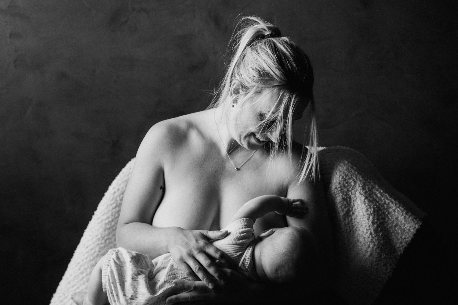 Black and white photo of a mother tenderly breastfeeding her newborn baby wrapped in a soft blanket.