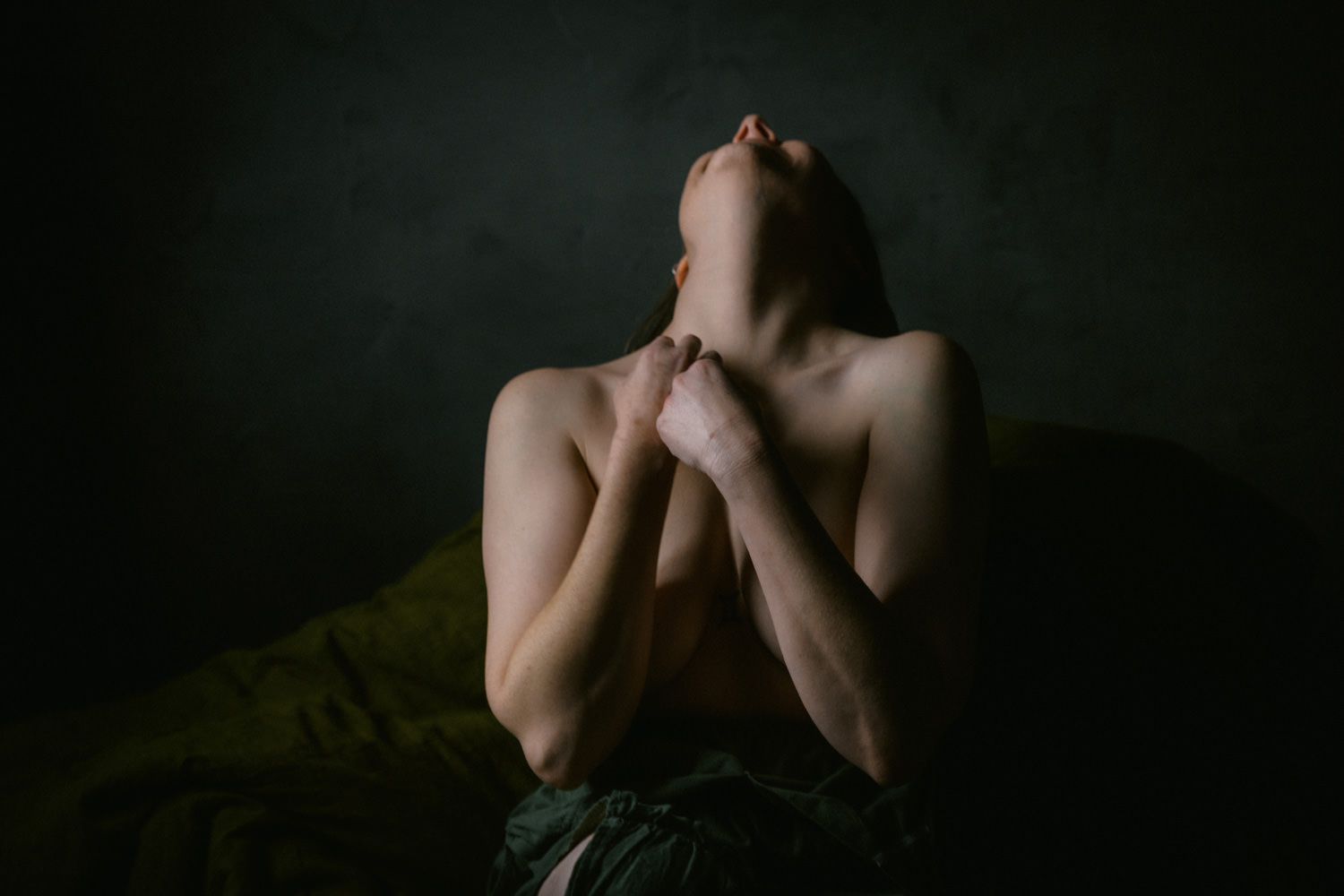 A person crosses their arms over their chest, head tilted back in a dramatic dark fine art pose.