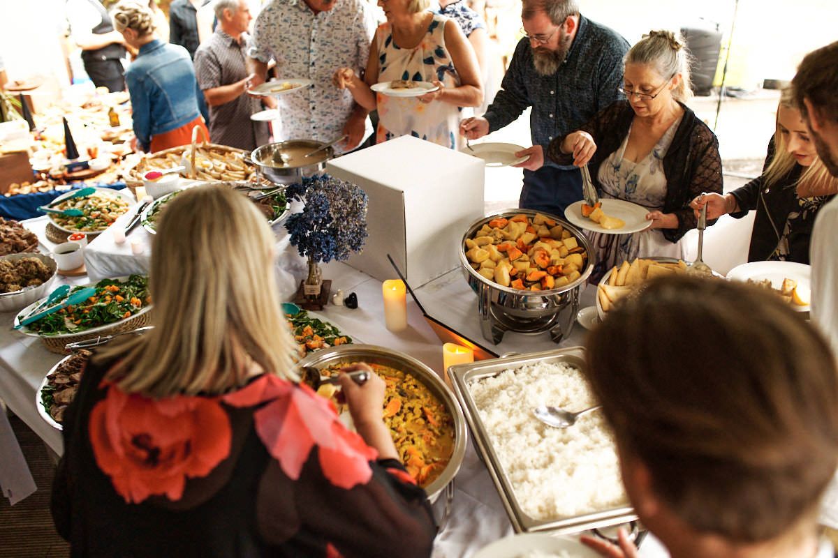 People serving themselves at a buffet table filled with various dishes at an outdoor catered event.