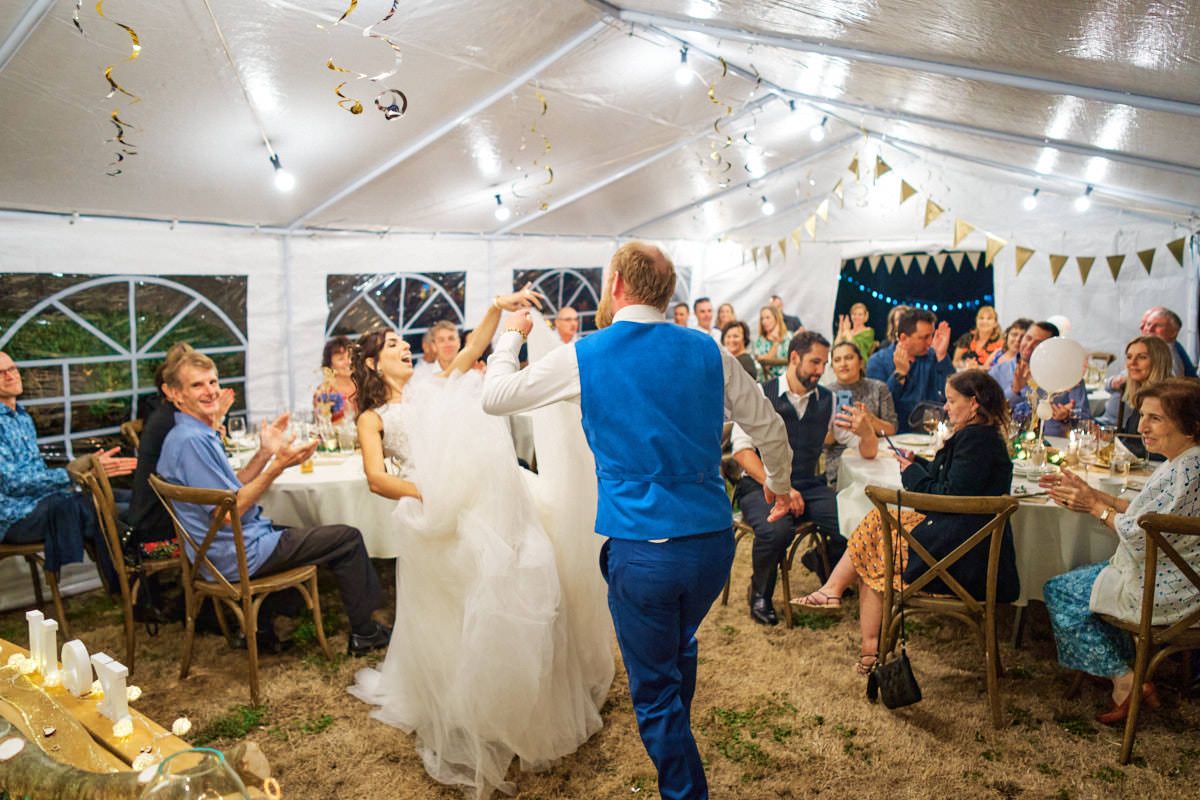 Bride and groom share first dance under a decorated tent at an elegant outdoor wedding reception.