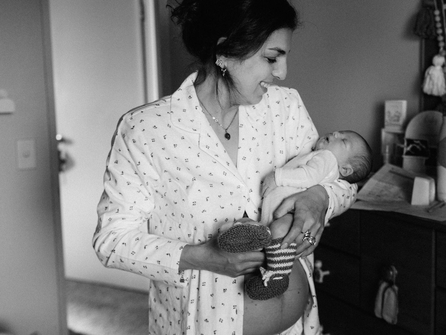 Black and white photo of a mother in a floral robe tenderly holding her newborn baby indoors.